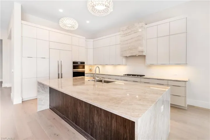 Kitchen featuring modern cabinets, light stone counters, a large island, white cabinets, and light wood-style floors
