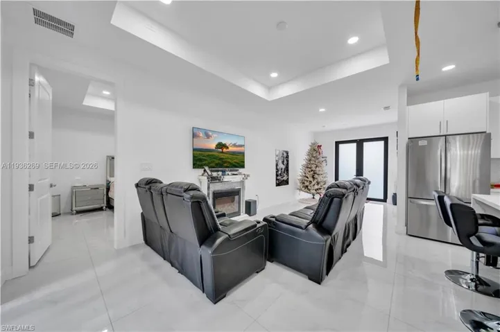 Living area with a tray ceiling, recessed lighting, french doors, and a glass covered fireplace