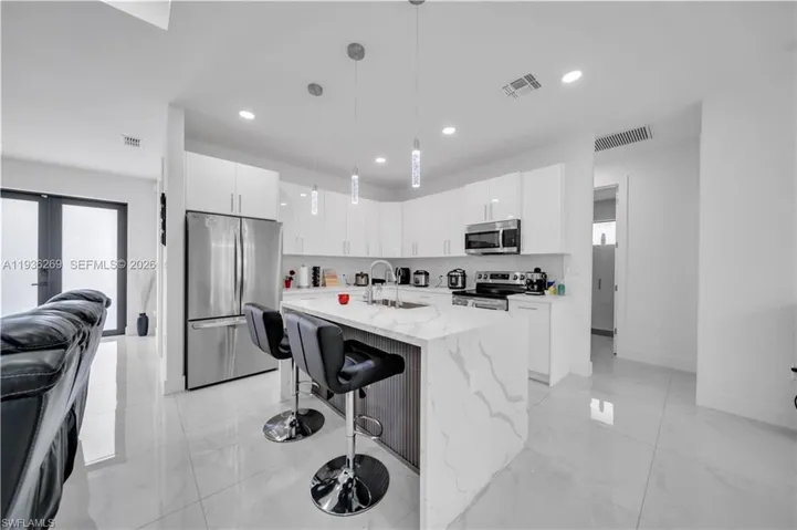 Kitchen featuring stainless steel appliances, a breakfast bar, white cabinets, an island with sink, and light stone counters