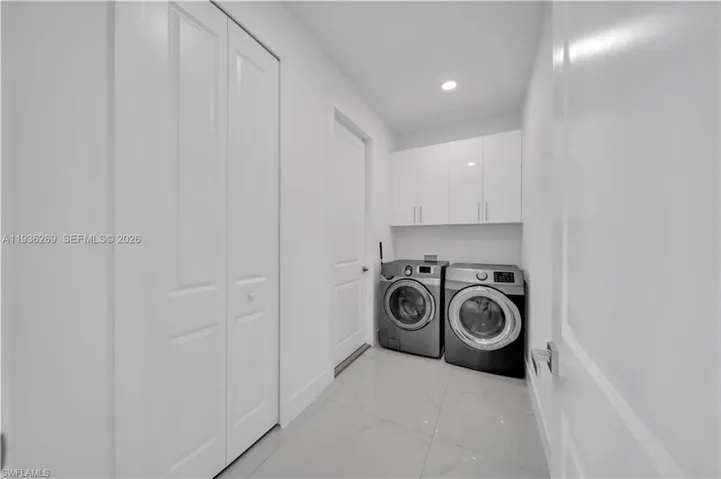Laundry room with washing machine and dryer, cabinet space, recessed lighting, and light marble finish floors