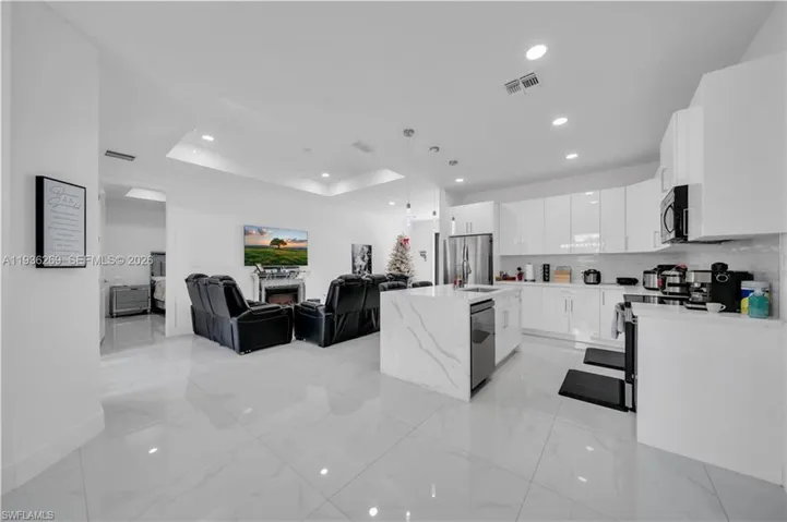 Kitchen with open floor plan, white cabinets, decorative light fixtures, light stone countertops, and backsplash