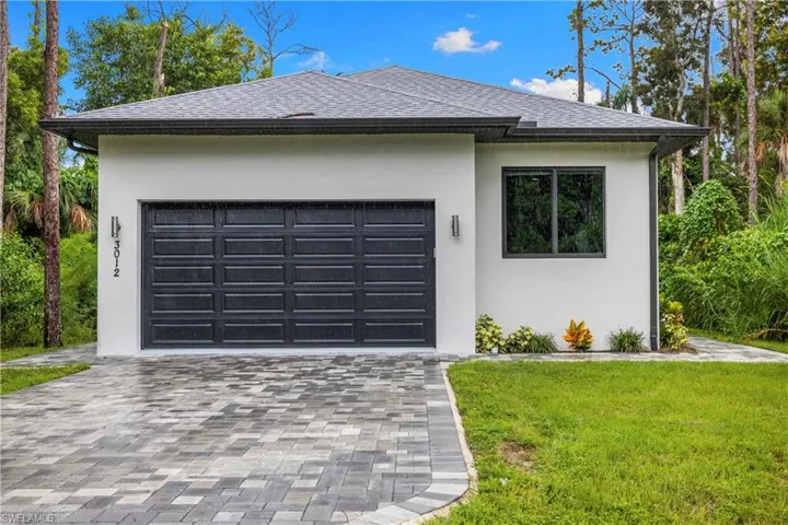 Contemporary facade featuring a dark gray paneled garage door, white stucco exterior, black-framed window, and a paver driveway