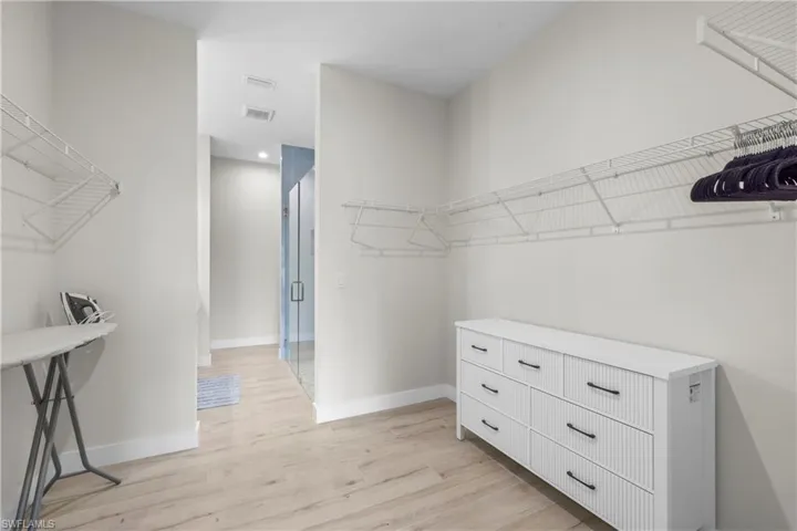 Spacious walk-in closet featuring light wood-finish flooring, white walls, and extensive wire shelving systems