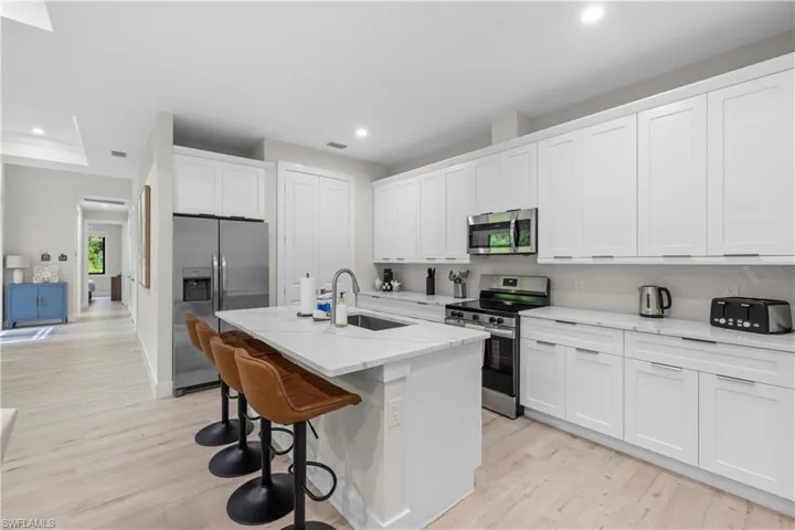 Kitchen featuring an island with a built-in sink, stainless steel appliances, white cabinetry, and light wood-finish flooring