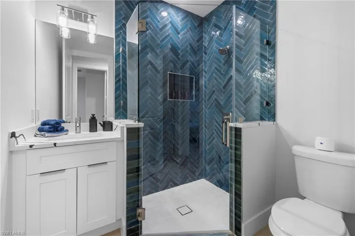Modern bathroom featuring a glass-enclosed shower with blue herringbone tile, a built-in shower niche, and a white vanity with integrated sink
