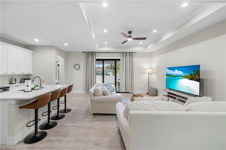 Open-concept living area with wood-finish flooring, recessed lighting, and a tray ceiling