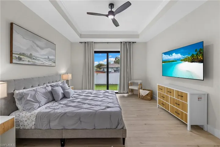 Spacious bedroom featuring wood-finish flooring, a tray ceiling with a modern ceiling fan, and direct access to the exterior through sliding glass doors