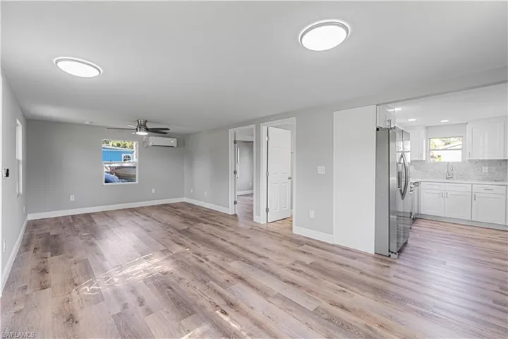 Unfurnished living room featuring light hardwood / wood-style flooring, plenty of natural light, an AC wall unit, and ceiling fan
