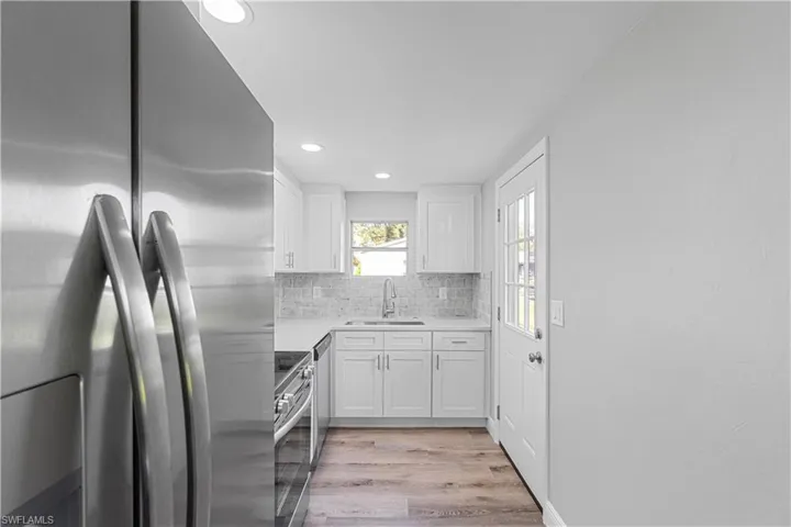 Kitchen featuring white cabinetry, sink, light hardwood / wood-style floors, decorative backsplash, and appliances with stainless steel finishes