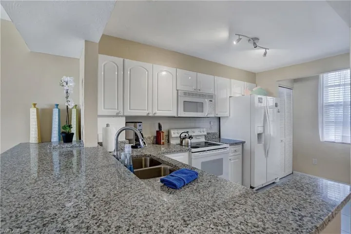 Kitchen with white cabinetry, white appliances, kitchen peninsula, track lighting, and sink