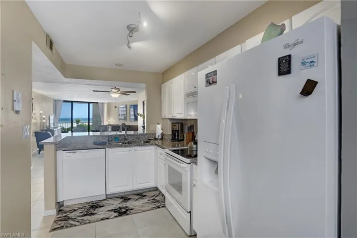 Kitchen with white cabinets, white appliances, sink, light tile patterned floors, and rail lighting