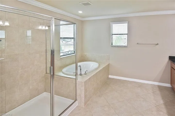 Bathroom featuring vanity, a bath, a stall shower, crown molding, and light tile patterned flooring