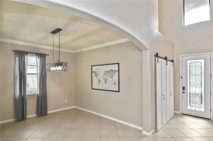 Foyer entrance featuring a barn door, arched walkways, light tile patterned flooring, and ornamental molding