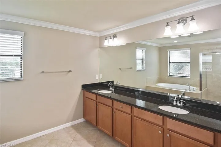 Bathroom featuring a bath, ornamental molding, double vanity, light tile patterned floors, and a tile shower