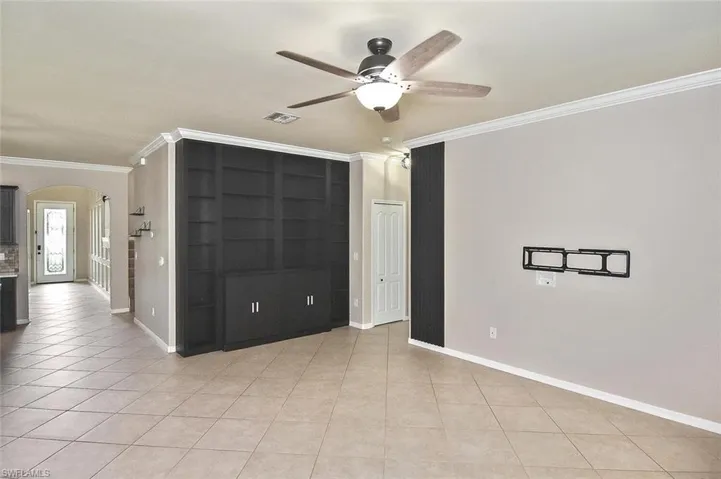 Empty room with crown molding, light tile patterned flooring, arched walkways, and a ceiling fan