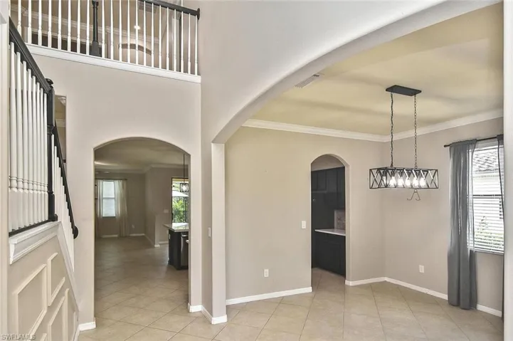 Unfurnished dining area with crown molding, light tile patterned floors, arched walkways, and a towering ceiling