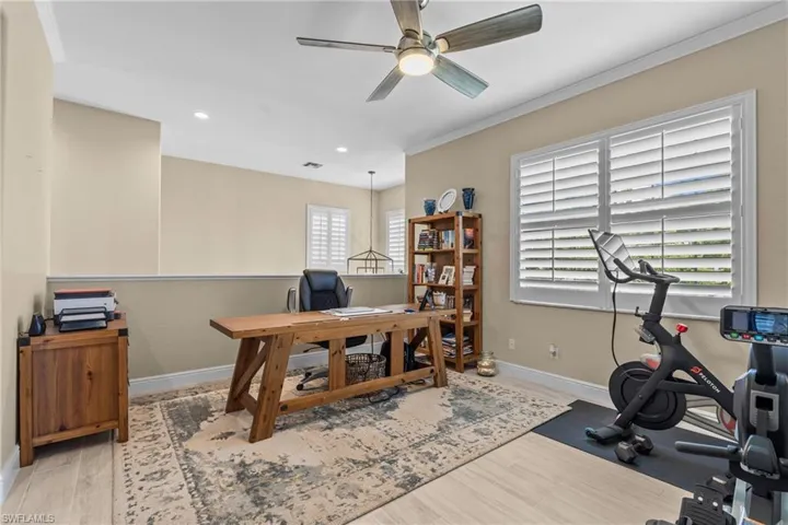 This versatile area features light-toned walls, crown molding, and a ceiling fan with integrated lighting