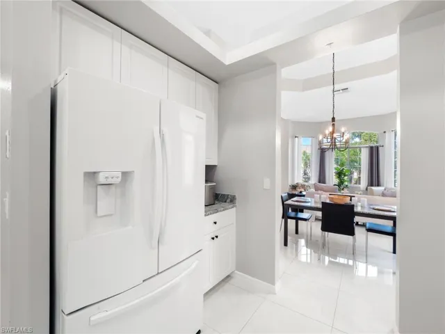 Kitchen featuring white refrigerator with ice dispenser, white cabinetry, a chandelier, light stone countertops, and light tile patterned flooring
