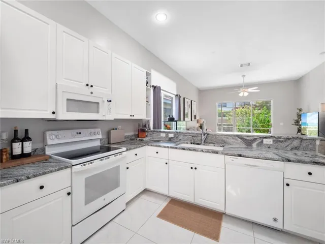 Kitchen with white appliances, white cabinets, dark stone counters, a ceiling fan, and light tile patterned flooring