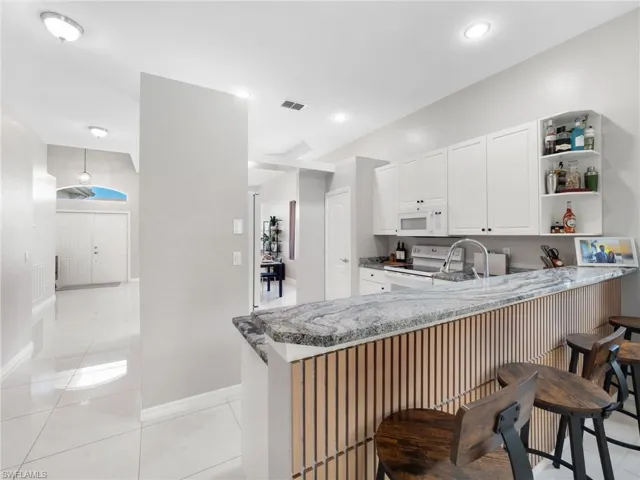 Kitchen featuring white cabinets, a peninsula, white appliances, open shelves, and light stone counters