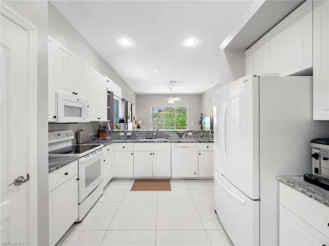 Kitchen featuring white appliances, white cabinets, dark stone counters, and recessed lighting