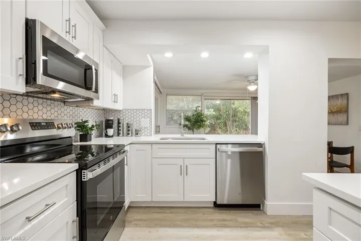 Kitchen with stainless steel appliances, a sink, decorative backsplash, light countertops, and light wood-type flooring