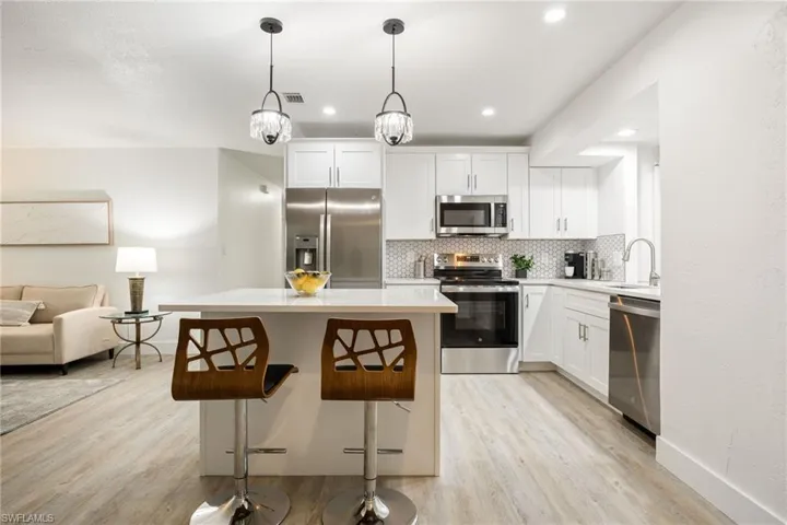 Kitchen with stainless steel appliances, light wood-type flooring, a sink, decorative backsplash, and recessed lighting