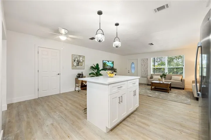 Kitchen featuring freestanding refrigerator, light wood finished floors, open floor plan, white cabinets, and decorative light fixtures