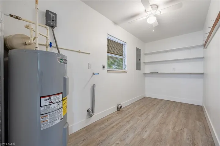 Laundry room with electric water heater, wood finished floors, a ceiling fan, electric panel, and baseboards