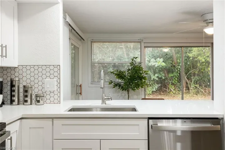 Kitchen featuring stainless steel dishwasher, a sink, tasteful backsplash, white cabinets, and ceiling fan
