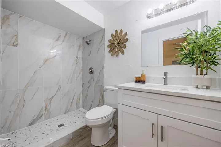 Bathroom featuring a tile shower, toilet, vanity, and wood finished floors