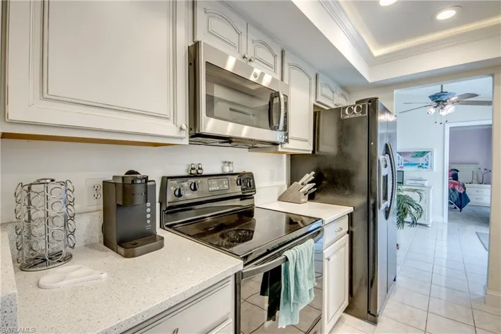 Kitchen featuring stainless steel appliances, ornamental molding, ceiling fan, a tray ceiling, and light tile patterned flooring