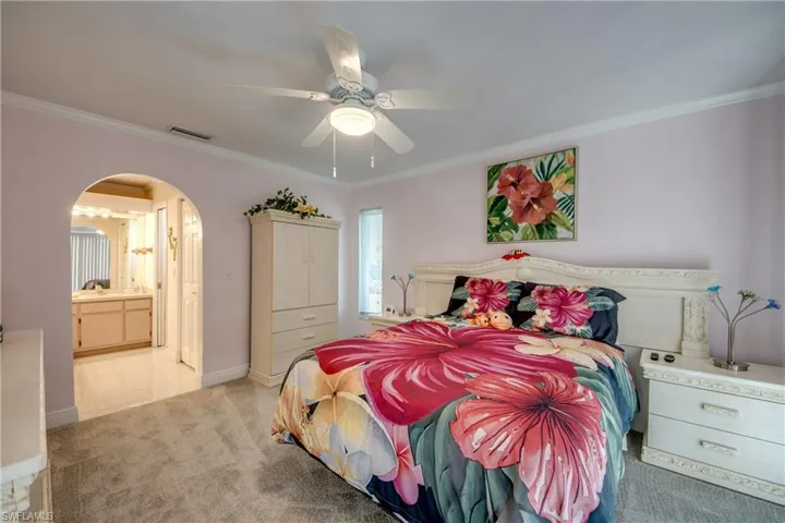 Bedroom with arched walkways, light colored carpet, ornamental molding, ceiling fan, and ensuite bathroom