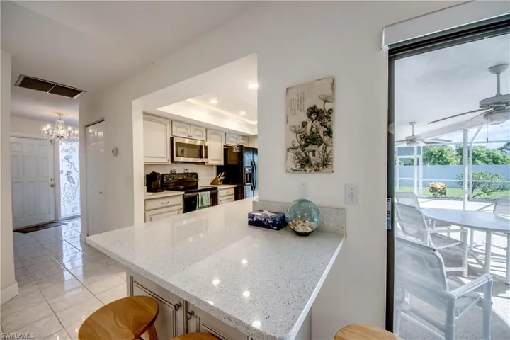 Kitchen with black appliances, a peninsula, a chandelier, light stone counters, and light tile patterned floors
