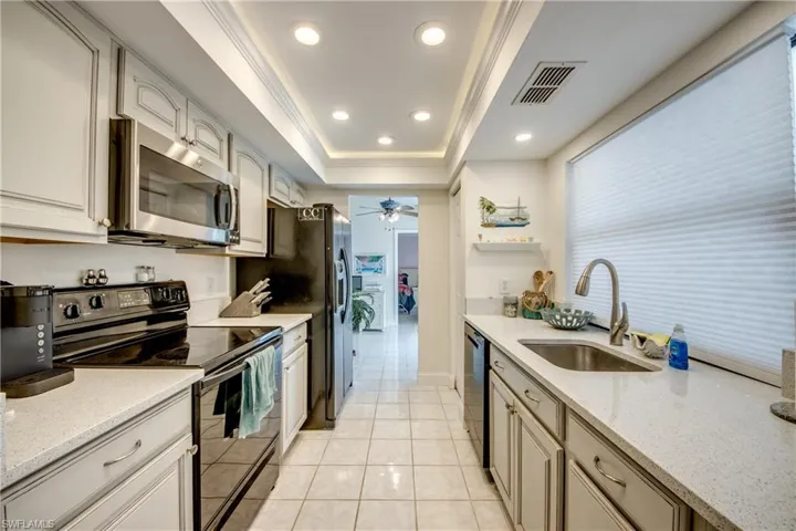 Kitchen featuring black appliances, a tray ceiling, light tile patterned flooring, light stone counters, and ceiling fan