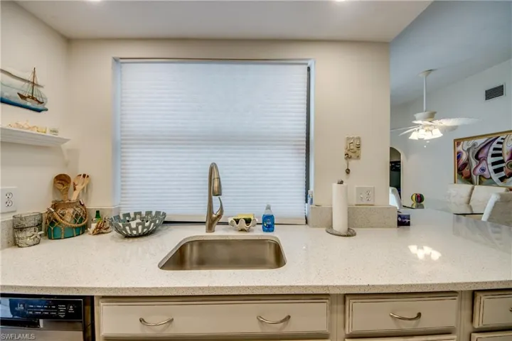 Kitchen featuring stainless steel dishwasher, light stone countertops, arched walkways, and a ceiling fan