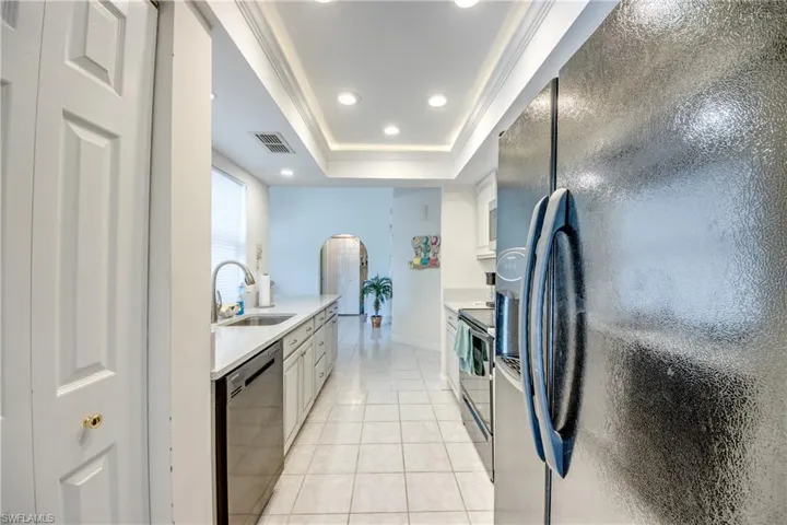 Kitchen with black appliances, arched walkways, a raised ceiling, light countertops, and light tile patterned floors