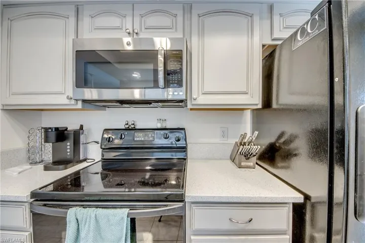 Kitchen with stainless steel appliances, white cabinets, light stone countertops, and tile patterned floors