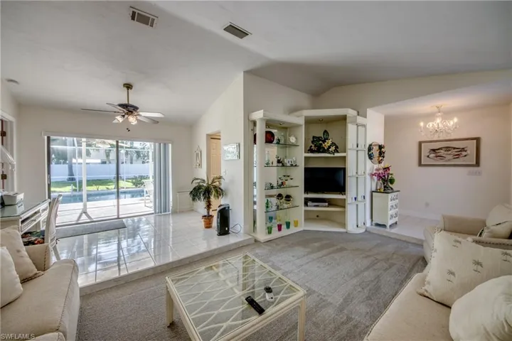 Living area featuring vaulted ceiling, carpet flooring, a chandelier, a ceiling fan, and tile patterned flooring