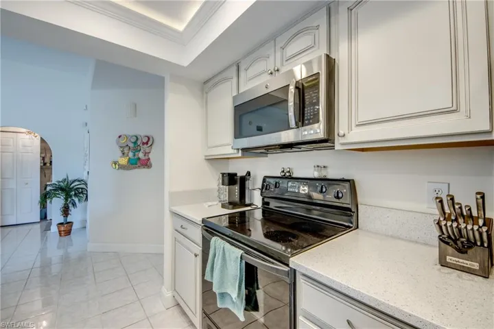 Kitchen with black electric range oven, stainless steel microwave, arched walkways, crown molding, and light stone counters