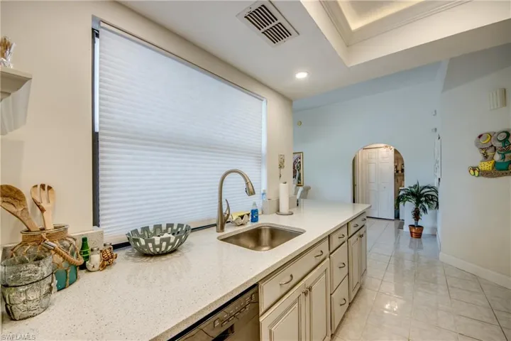 Kitchen featuring arched walkways, cream cabinetry, black dishwasher, light stone counters, and recessed lighting
