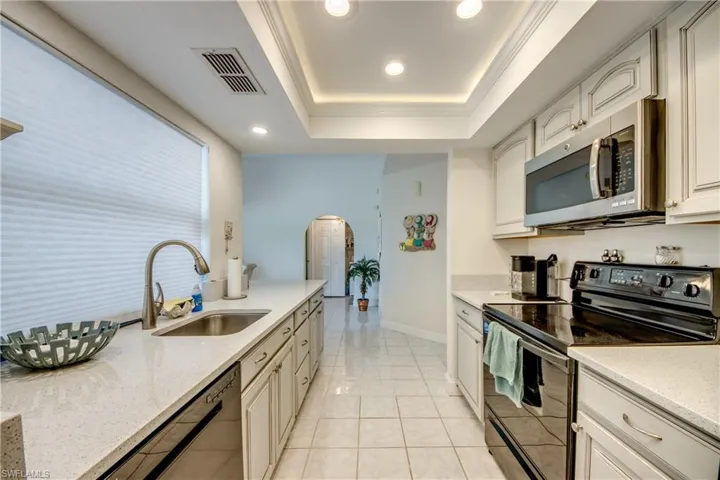 Kitchen featuring black range with electric stovetop, stainless steel microwave, arched walkways, a raised ceiling, and dishwasher
