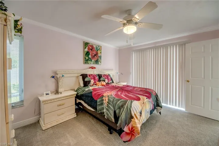 Bedroom with ornamental molding, light carpet, multiple windows, and a ceiling fan