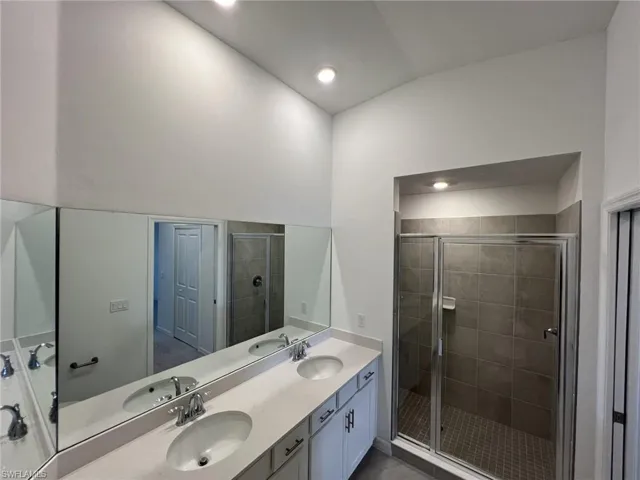 Bathroom with a shower stall, double vanity, recessed lighting, and dark tile patterned flooring