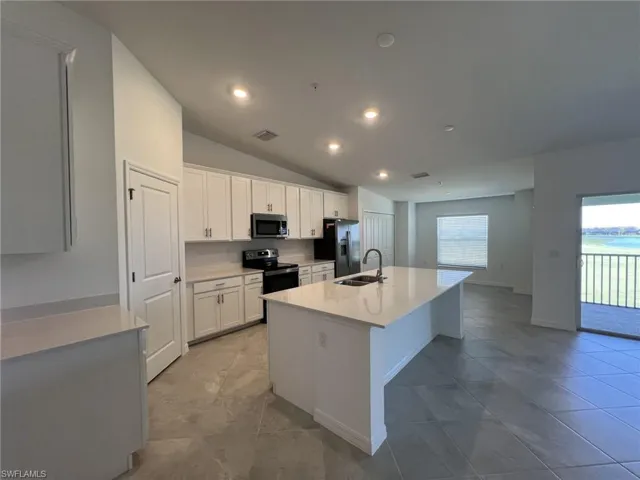Kitchen featuring an island with sink, vaulted ceiling, white cabinets, appliances with stainless steel finishes, and light stone counters