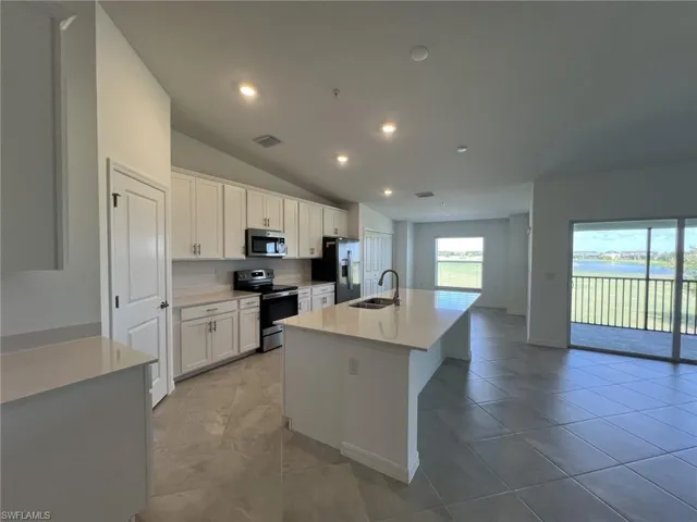 Kitchen featuring a center island with sink, appliances with stainless steel finishes, lofted ceiling, white cabinetry, and a breakfast bar area