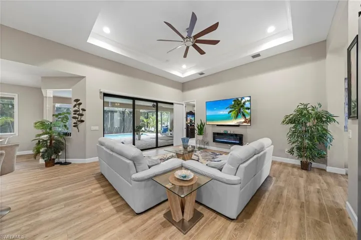 Living room featuring a barn door, light wood finished floors, a ceiling fan, an office area, and a glass covered fireplace