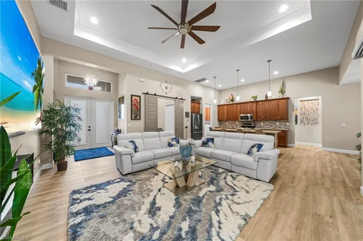 Living area featuring a tray ceiling, wood finished floors, recessed lighting, a ceiling fan, and a glass covered fireplace