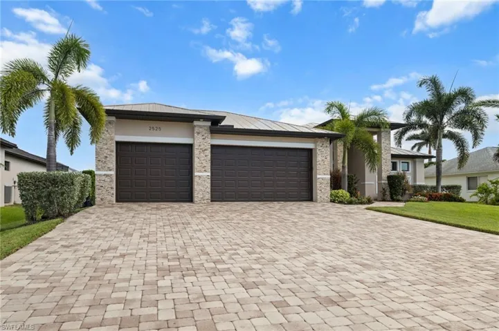 View of front of home featuring an attached garage, stone siding, decorative driveway, stucco siding, and a front yard
