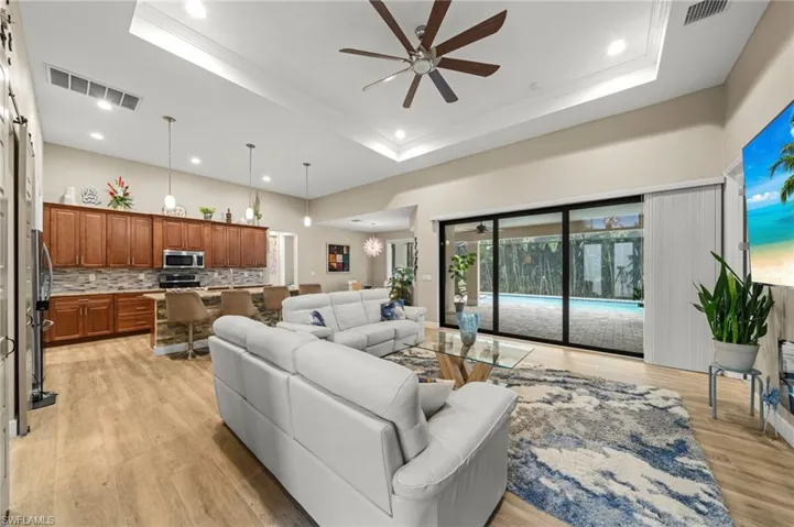 Living room with a tray ceiling, light wood finished floors, a ceiling fan, recessed lighting, and a glass covered fireplace